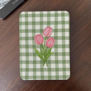 May include: A rectangular case with a green and white gingham pattern. The case features a watercolor illustration of three pink tulips with green leaves. The case is likely for an e-reader.