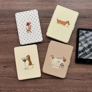 Può includere: Quattro custodie rettangolari per e-reader con illustrazioni di bassotti. Una è bianca a pois neri con un cane con basco. Due sono color crema con cani che bevono da bicchieri. Una è beige con un cane in un bagno di schiuma. Un e-reader è visibile.