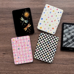 May include: Four rectangular e-reader cases and one black e-reader device. One case is black with a sun and two dragonflies. One is white with colorful stars. One is pink and white gingham with small stars. One is black and white checkered.