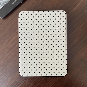 May include: A rectangular e-reader cover featuring a cream-colored background with a repeating pattern of small, evenly spaced black polka dots. The cover has rounded corners and a smooth, flat surface, shown from a direct top-down perspective.