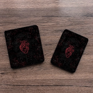 May include: Two rectangular coasters with a black background featuring a red anatomical heart illustration centered over a faint outline of a rose. The design includes subtle red splatter patterns across the dark surface of both items.