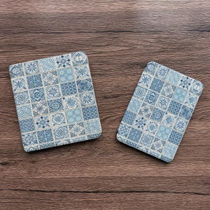 Puede incluir: Dos posavasos rectangulares con un patrón de baldosas azules y blancas. El diseño presenta varias formas florales y geométricas en tonos azules. Los posavasos se muestran sobre una superficie de madera.