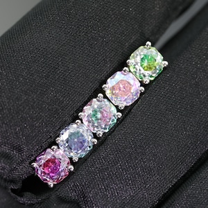 May include: A line of five square-cut, iridescent gemstones in a silver setting. The gemstones display a range of colours, including pink, purple, green, and yellow. The jewellery is set against a black background.