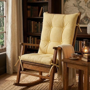May include: A wooden rocking chair featuring a tufted, yellow and white striped cushion secured with fabric ties. The chair has curved rockers, armrests, and a high backrest. A cream-coloured throw blanket is draped over the side of the seat.