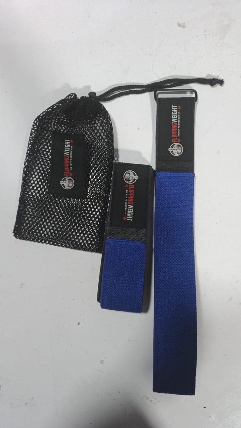 Puede incluir: Una bolsa de malla negra y dos correas de ejercicio azules con el texto "FLIPPING WEIGHT" en rojo y blanco. Las correas est&aacute;n hechas de un material texturizado y tienen una banda negra con el mismo texto. La bolsa se cierra con un cord&oacute;n negro.