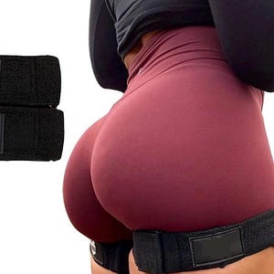 Puede incluir: Bandas de resistencia negras en el lado izquierdo. Las bandas están hechas de un material tejido. Una persona lleva pantalones cortos burdeos y una camiseta negra de manga larga. Una banda de resistencia negra está envuelta alrededor del muslo.