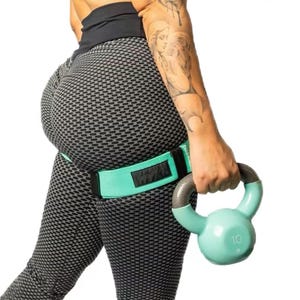 Puede incluir: Una persona con leggings grises texturizados y una banda de resistencia para la cadera verde claro. La persona sostiene una pesa rusa verde claro con un asa gris. La pesa rusa está marcada con el número 10.