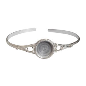 May include: Silver-toned cuff bracelet with an open design. The bracelet features a central circular setting with a textured edge, ideal for adding a decorative element. The band has decorative flourishes on either side of the central setting.