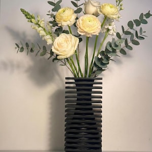 Puede incluir: Una taza de cerámica blanca con un asa negra y el texto "But First, Coffee" en negro y negrita. La taza está sobre una superficie blanca. La taza mide aproximadamente 10 cm de alto.