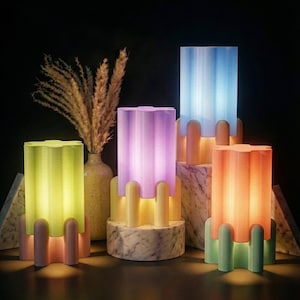 Pode incluir: Uma coleção de luminárias modernas e coloridas com um design único. Cada luminária apresenta uma cúpula cilíndrica e canelada em tons de verde, roxo, azul e laranja, apoiada em uma base com um suporte arqueado decorativo. As luminárias estão iluminadas, criando um brilho quente.