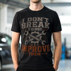 May include: A black short-sleeved t-shirt featuring a graphic print with the text I DON'T BREAK THINGS I IMPROVE THEM. The design includes a central illustration of two crossed metal wrenches positioned over a gear icon in a distressed style.