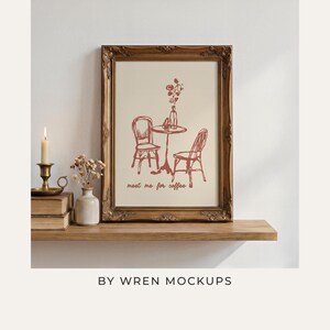 A4 ornate wood frame mockup styled on a warm wooden shelf with vintage books, a lit taper candle in a brass holder, and dried florals in a small ceramic vase, evoking old-world cottagecore charm. Overlay text reads "By Wren Mockups."