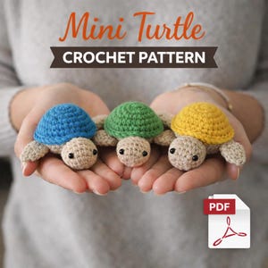 以下が含まれることがあります： 青、緑、黄色の3匹のかぎ針編みのミニカメが、すぼめた手の中に収められています。カメはベージュの頭と手足、黒い目です。画像には「Mini Turtle CROCHET PATTERN」というテキストとPDFアイコンが含まれています。
