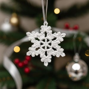 May include: A white, crocheted snowflake Christmas tree ornament suspended by a white ribbon. The snowflake, with its intricate openwork design, is the focal point. The background is blurred, featuring a decorated Christmas tree.