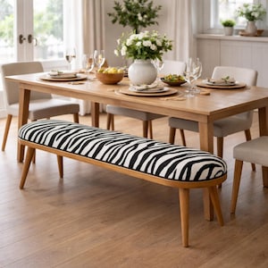 Puede incluir: Un comedor con una mesa de madera y un banco con estampado de cebra. La mesa está puesta con platos y vasos. El banco tiene un patrón en blanco y negro. La habitación tiene un ambiente luminoso y espacioso.