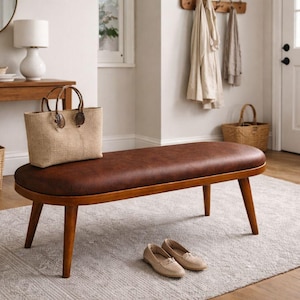 May include: A brown leather bench with wooden legs, a woven tote bag, and a pair of beige flats. The bench is in a well-lit entryway with a rug, a side table, and a round mirror. A basket and a lamp are also visible.