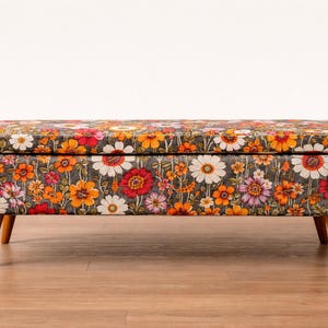 May include: A rectangular storage ottoman with a floral pattern in shades of orange, red, white, and purple on a dark gray background. The ottoman has wooden legs and a hinged lid. The dimensions are approximately 48 inches long, 18 inches wide, and 16 inches high.