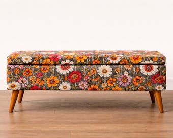 Puede incluir: Un otomán rectangular con estampado floral en tonos naranja, rojo, blanco y morado sobre un fondo gris oscuro. El otomán tiene patas de madera y una tapa con bisagras. Las dimensiones son de aproximadamente 122 cm de largo, 46 cm de ancho y 41 cm de alto.