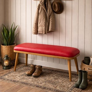 May include: A red bench with a wooden frame and legs. A tan jacket and hat hang on a wooden rack above. Brown boots and green wellington boots are on a patterned rug. The bench is approximately 120 cm long.