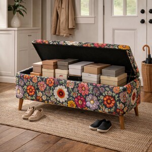 May include: A floral storage bench with a dark background and colorful flowers. The bench is open, revealing several boxes inside. Two pairs of shoes sit in front of the bench on a jute rug.