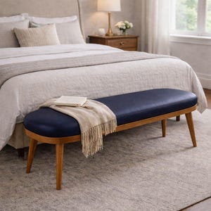 Puede incluir: Un banco tapizado azul marino con estructura de madera y patas anguladas. Una manta beige y un libro descansan sobre el banco. El banco está en un dormitorio con una cama y una alfombra.