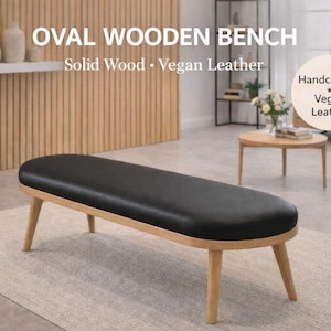 May include: Oval wooden bench with a black vegan leather seat and solid wood frame. The bench has a rounded oval shape and four angled legs. The text on the image says "Solid Wood • Vegan Leather" and "Handcrafted Vegan Leather".