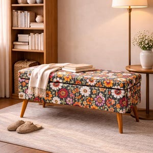 May include: A rectangular storage bench with a floral pattern in shades of orange, red, pink, and white on a dark background. The bench has wooden legs and is topped with a cream-colored throw and books. A pair of slippers sits on the rug.