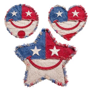 Pode incluir: Três decorações patrióticas de tecido em forma de círculo, coração e estrela. Cada uma tem um esquema de cores azul e vermelho com uma estrela branca e um sorriso costurado. As bordas são desfiadas, dando um aspecto rústico.