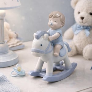 Könnte beinhalten: Eine Keramikfigur eines Babys auf einem weiß-blauen Schaukelpferd. Das Baby trägt einen blauen Anzug und hat einen Schnuller. Ein blau-weißer Schnuller liegt daneben. Ein weißer Teddybär mit blauer Schleife ist im Hintergrund.