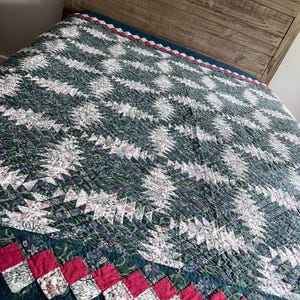 May include: A quilted bedspread featuring a pineapple-inspired geometric pattern in shades of dark green, white, and floral prints. The border consists of a vibrant red and white checkered design, with intricate stitching throughout the fabric.