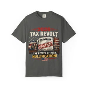 May include: Dark gray t-shirt with a distressed graphic. The graphic includes the text "2026 TAX REVOLT" above an image of an IRS warrant marked "NULLIFIED!" and the words "THE POWER OF JURY NULLIFICATION!" with an American flag.