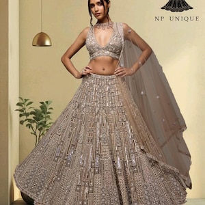 May include: A beige formal gown with detailed beadwork and a matching sheer veil. The gown has a plunging neckline and a full skirt with geometric patterns. The text "NP UNIQUE" is visible on the upper right.