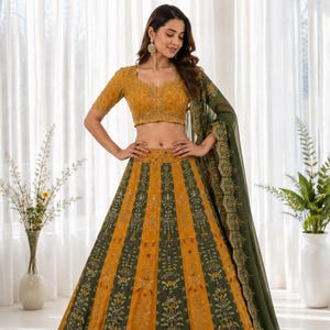 May include: A mustard yellow and olive green lehenga choli set featuring a cropped blouse with short sleeves and a floor-length skirt with alternating vertical panels of floral embroidery and intricate patterns, paired with a sheer olive dupatta.