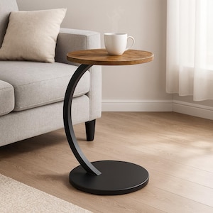 Puede incluir: Una pequeña mesa auxiliar redonda con una tapa de madera marrón oscuro y una base de metal negro curvada. Una taza blanca está sobre la mesa y un sofá gris en el fondo. La mesa mide aproximadamente 51 cm de altura.