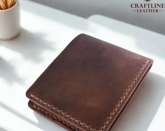 May include: A brown leather wallet with white stitching around the edges. The wallet is square and appears to be folded. The Craftline Leather logo is visible in the upper right corner.