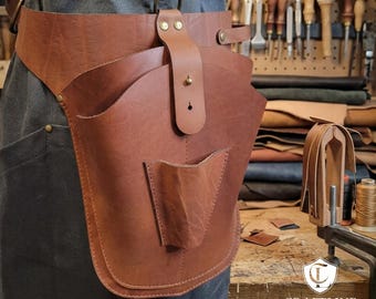 May include: A brown leather tool belt with multiple pockets and a brass ring. The belt is worn around the waist and has a small pocket on the front. The Craftline Leather logo is visible in the bottom right corner.