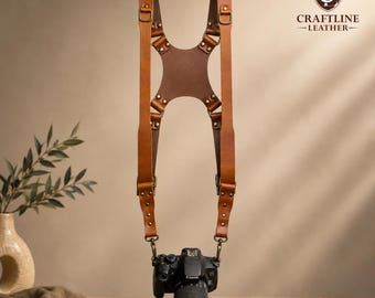 May include: A brown leather camera harness with adjustable straps and metal hardware. The harness is designed to hold a camera, which is attached at the bottom. The brand name "CRAFTLINE -LEATHER-" is visible on the right side.