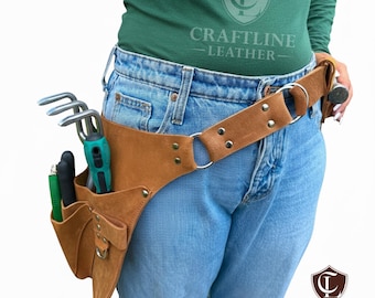May include: A brown leather gardening tool belt with multiple pockets and a metal ring. The belt is worn around the waist and holds various gardening tools, including a trowel and hand rake. The Craftline Leather logo is visible.