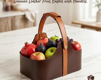 Könnte beinhalten: Ein brauner Leder-Obstkorb mit beigem Griff und Akzenten, gefüllt mit einer Vielzahl frischer Früchte, darunter Granatäpfel, Äpfel, Feigen und Trauben. Der Text "Genuine Leather Fruit Basket with Handles" ist zu sehen.