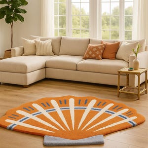 Könnte beinhalten: Orangefarbener, fächerförmiger Teppich mit weißen und blauen Akzenten. Der Teppich liegt auf einem Holzboden vor einem beigefarbenen Ecksofa. Der Raum hat große Fenster und eine neutrale Farbpalette.