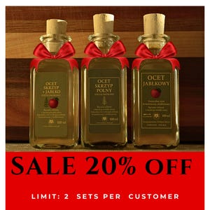 Op de afbeelding: Drie glazen flessen azijn met kurken en rode strikken. Elke fles heeft een etiket met Poolse tekst en een rode appelillustratie. De tekst "SALE 20% OFF" wordt weergegeven op een rode banner.