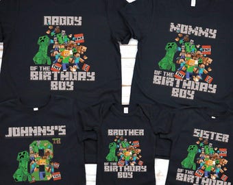 Op de afbeelding: Zwarte T-shirts met Minecraft-thema graphics. De shirts tonen teksten als "Papa", "Mama", "Broer", "Zus" en "Verjaardagsjongen". Elk shirt heeft een Minecraft-karakterontwerp met de tekst "Of The Birthday Boy".