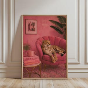 Op de afbeelding: Een ingelijste kunstdruk met een jachtluipaard die rust op een roze schelpvormige fauteuil. Op een kleine ronde tafel staan een roze mok en drie gestapelde boeken met de titels Ibiza Bliss, Capri Dolce Vita en Marrakesh Flair.