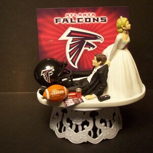 Könnte beinhalten: Eine Tortenaufsatz für eine Hochzeit mit dem Thema Atlanta Falcons. Der Bräutigam entspannt sich mit einem Football, Helm und Fernbedienung. Der Hintergrund zeigt das Logo der Atlanta Falcons. Die Kuchenbasis hat ein dekoratives Design.