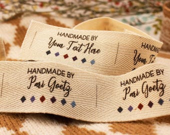 May include: Close-up of beige fabric labels with the text "HANDMADE BY Your Text Here" and "HANDMADE BY Pari Goetz" in black script. Each label has a row of small, colorful diamond shapes.