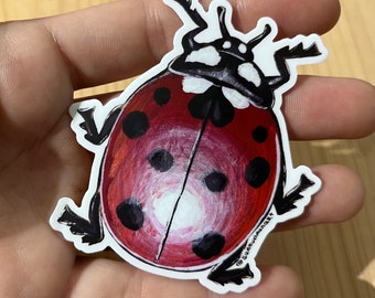 May include: A red ladybug sticker with black spots and white accents. The ladybug is drawn in a realistic style with details like its antennae and legs. The sticker has a white border and the text "@sunflowerwandart" in the bottom right corner.
