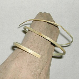 May include: A set of three woven, light brown, twig bracelets. The bracelets are coiled and stacked on top of each other.