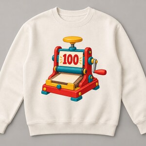 May include: A cream-colored crewneck sweatshirt featuring a central graphic of a red, blue, and yellow mechanical press machine. The machine has a hand crank on the side and a white paper sheet in the center with the number 100 printed in red.
