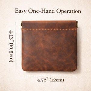 May include: A brown leather coin purse with a rectangular shape. The purse is 4.72 inches (12 cm) wide and 4.13 inches (10.5 cm) tall. The text "Easy One-Hand Operation" is at the top. The purse has a stitched seam and metal accents.