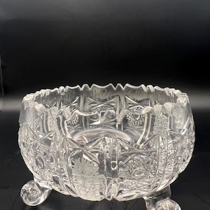 Peut inclure: Un bol en verre taillé transparent avec un bord festonné et trois pieds arrondis. Le bol présente des motifs géométriques complexes et des motifs d'éclats d'étoiles, créant un effet scintillant. Ce bol décoratif est idéal pour servir ou exposer.